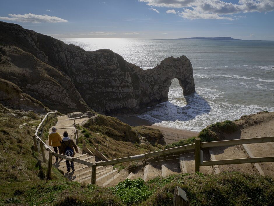 Deux personnes descendant les marches de la plage de Durdle Door lors d'une journée ensoleillée en mars, Dorset, Royaume-Uni