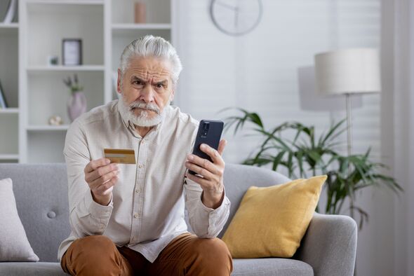 Un homme âgé bouleversé tient un téléphone et une carte de crédit