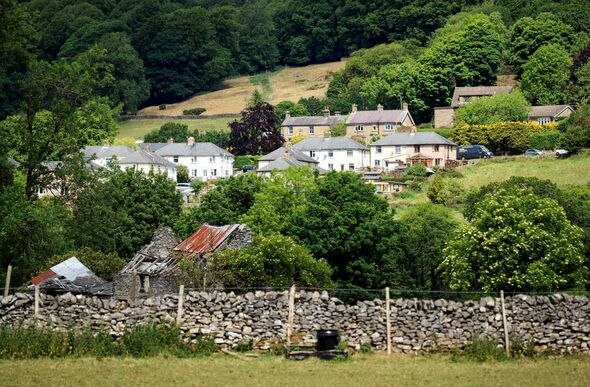 Une vue aérienne d'un village rural, niché dans une vallée verdoyante entourée d'une verdure luxuriante et de collines, présente une collection