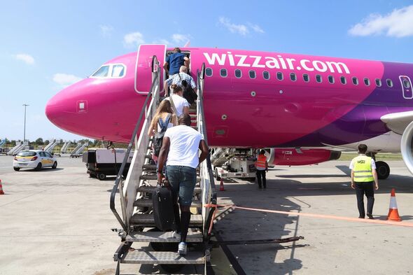 Des individus montent à bord d’un avion rose et violet, probablement un avion commercial, dans un aéroport. L'avion affiche les toiles