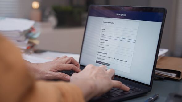 Gros plan sur le remplissage des formulaires fiscaux sur un ordinateur portable tout en examinant les documents pour la déclaration de revenus en ligne, la gestion financière et l'administration Gros plan sur le remplissage des formulaires fiscaux sur un ordinateur portable tout en examinant les documents pour la déclaration de revenus en ligne, la gestion financière et l'administration