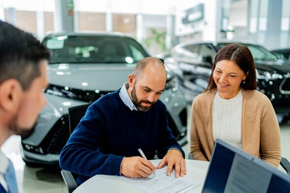 Couple signant des documents chez un concessionnaire automobile Couple signant des documents chez un concessionnaire automobile