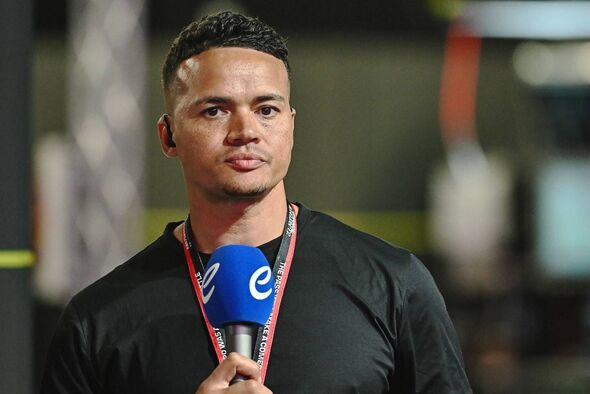 Un individu vêtu d'un t-shirt noir se tient debout, tenant un microphone, peut-être en train de participer à une interview ou à une présentation.