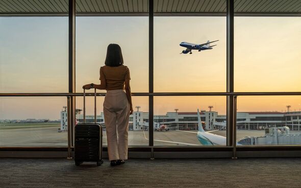 Une femme se tient près de la fenêtre d’un aéroport et regarde un avion décoller sur fond de coucher de soleil. Elle tient un su Une femme se tient près de la fenêtre d’un aéroport et regarde un avion décoller sur fond de coucher de soleil. Elle tient un su