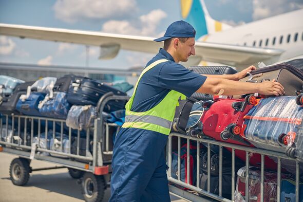 Vue latérale d'un jeune homme caucasien sérieux en uniforme chargeant des valises de l'avion sur les chariots Vue latérale d'un jeune homme caucasien sérieux en uniforme chargeant des valises de l'avion sur les chariots