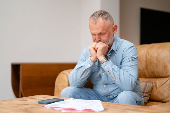 Homme assis sur un canapé avec des documents semblant inquiet dans un salon moderne