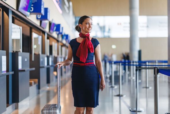 Joyful Mid Adult Caucasian Hôtesse de l'air manœuvrant des bagages à roulettes grâce à l'enregistrement à l'aéroport