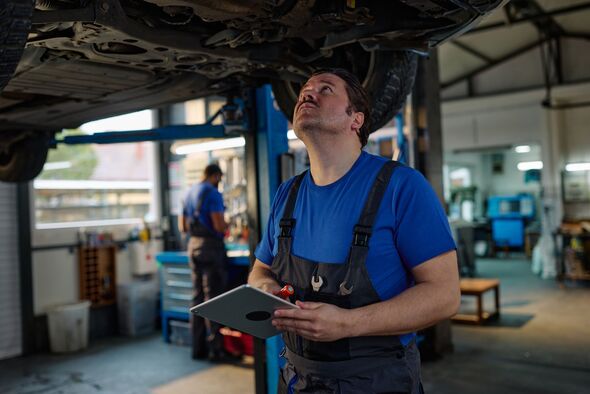 Mécanicien automobile inspectant le train de roulement du véhicule dans un atelier très fréquenté à l'aide d'une tablette pour les notes de diagnostic