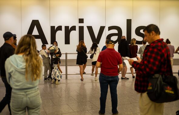 Les gens attendent pour saluer amis et parents à côté d'un énorme panneau indiquant les arrivées à l'aéroport d'Heathrow, terminal 4, Londres, Royaume-Uni.