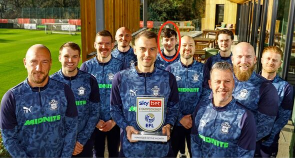 Un groupe d'individus vêtus de maillots bleus assortis avec des accents verts, debout ensemble avec un grand trophée au milieu.