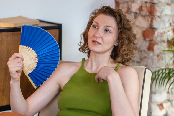Femme surchauffée utilisant un ventilateur en papier pour soulager l'état de congestion à la maison sans climatiseur.