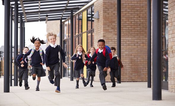 Des écoliers du primaire, portant des uniformes scolaires et des sacs à dos, courant sur une passerelle à l'extérieur de leur bâtiment scolaire, vue de face