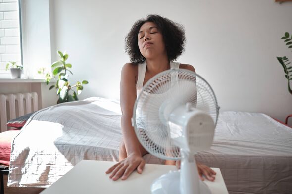 Fatiguée, épuisée, une femme afro-américaine souffrant de chaleur pendant la saison estivale, assise devant un ventilateur électrique, vivant à l'apa