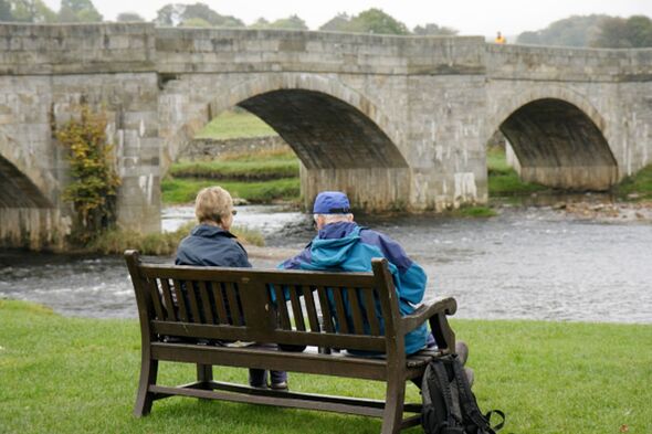 Un couple était assis sur un banc à côté de la rivière Whafe à Burnsall.